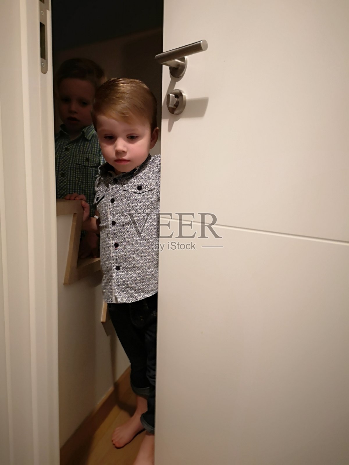 蹒跚学步的孩子淘气,躲在门后照片摄影图片