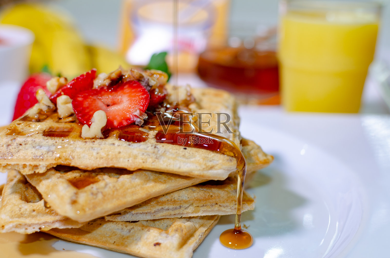 健康早餐——由小麦奶油制成的华夫饼,配上草莓、核桃、蜂蜜、香蕉和新鲜果汁照片摄影图片