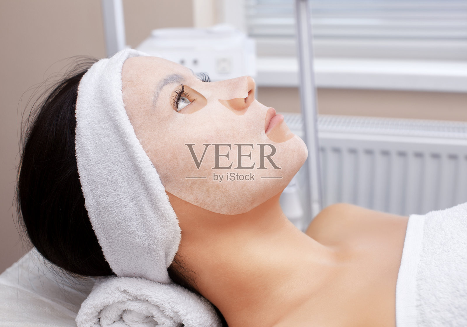 美容师在美容院给一位年轻女士敷面膜,以清洁和滋润皮肤。照片摄影图片