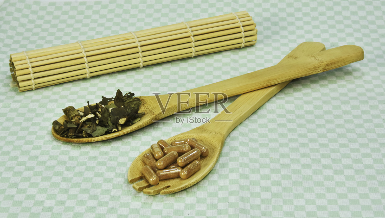 在绿色的自然背景下,用竹制的木勺盛着绿茶的叶子和胶囊。照片摄影图片