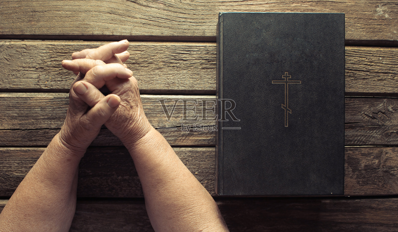 老妇人的双手祈祷在古老的乡村木板上的圣经书。宗教的概念照片摄影图片