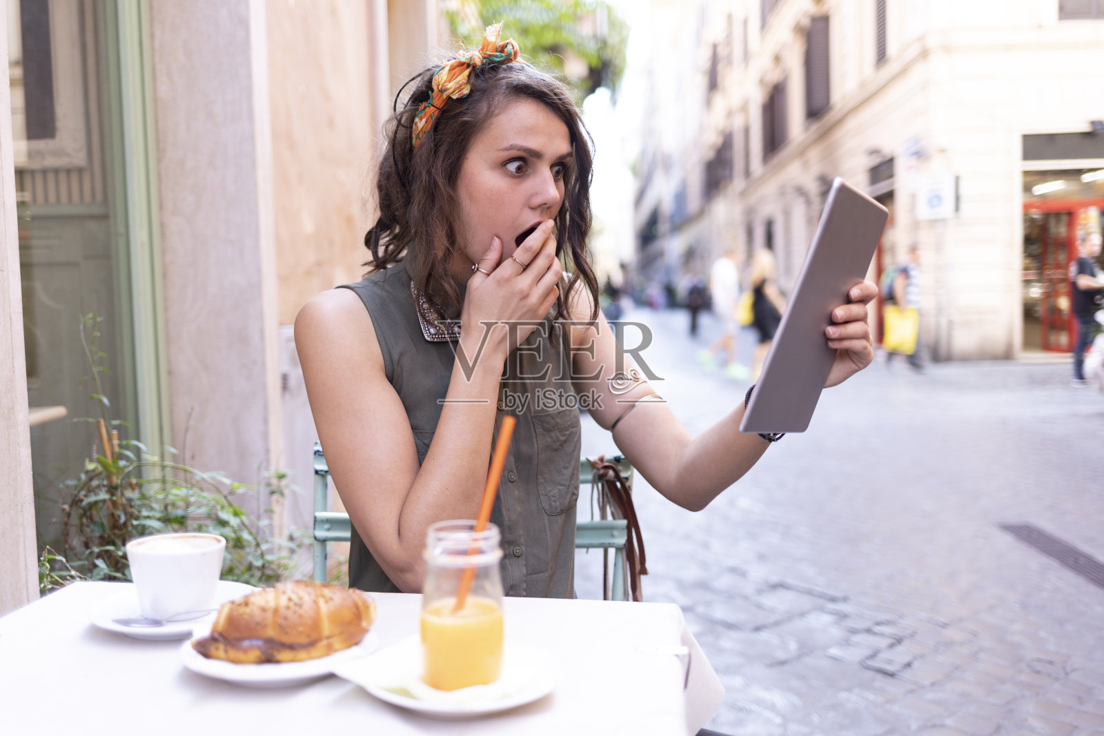 惊讶的女人在户外吃早餐,看着平板电脑照片摄影图片