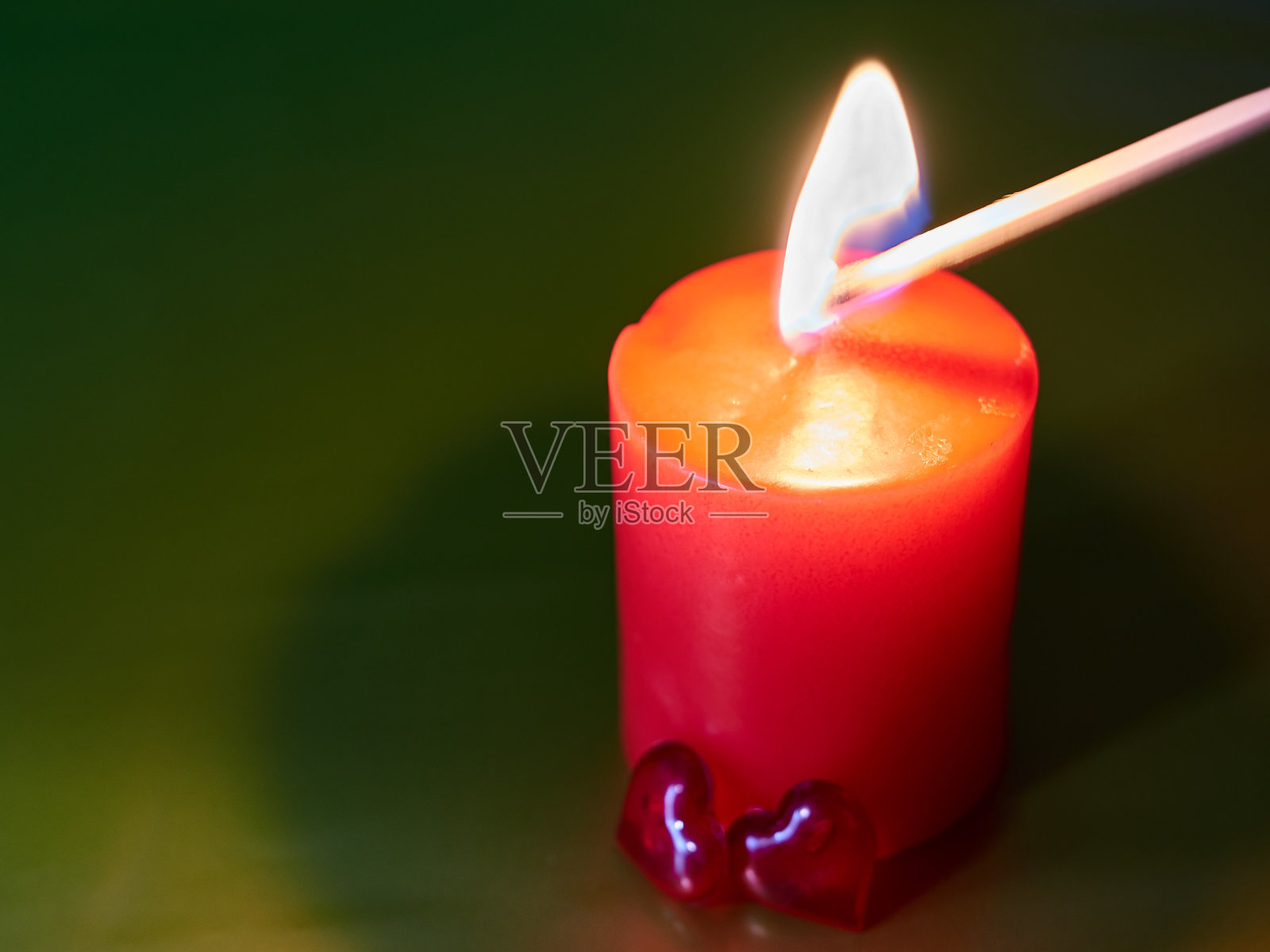 绿色装饰背景上的红色浪漫蜡烛,两颗红色玻璃心并排站着,一根火柴点燃蜡烛。爱的象征。节日的气氛中。浪漫晚餐。照片摄影图片