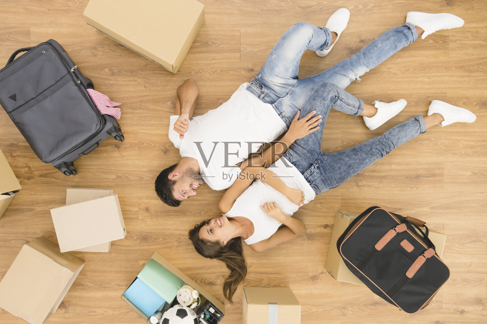 这对微笑的夫妇躺在箱子旁边的地板上。从上面的观点照片摄影图片