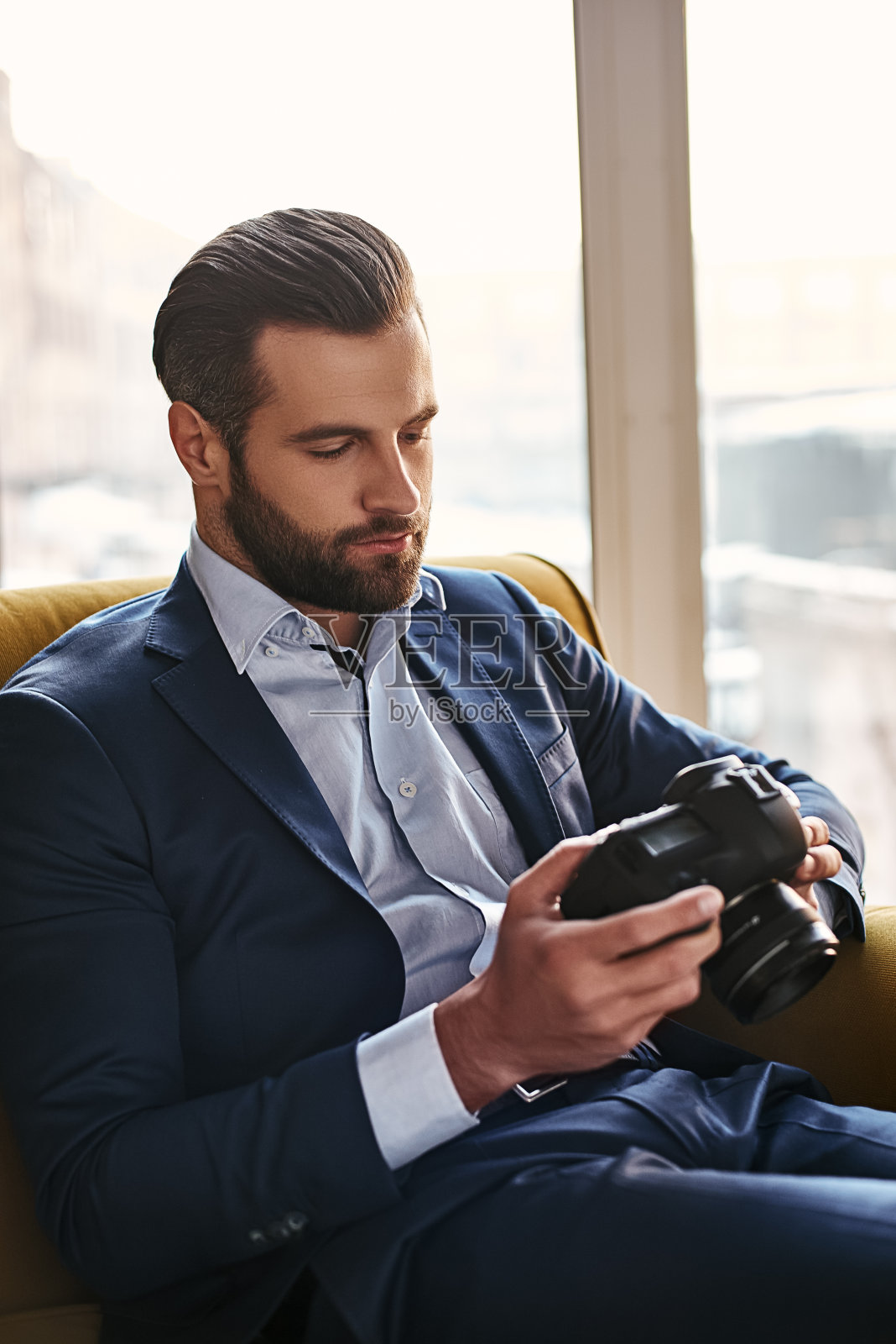 摄影是一个伟大的爱好…近距离的肖像年轻的胡子和穿着很好的商人谁是看照片上的相机。照片摄影图片