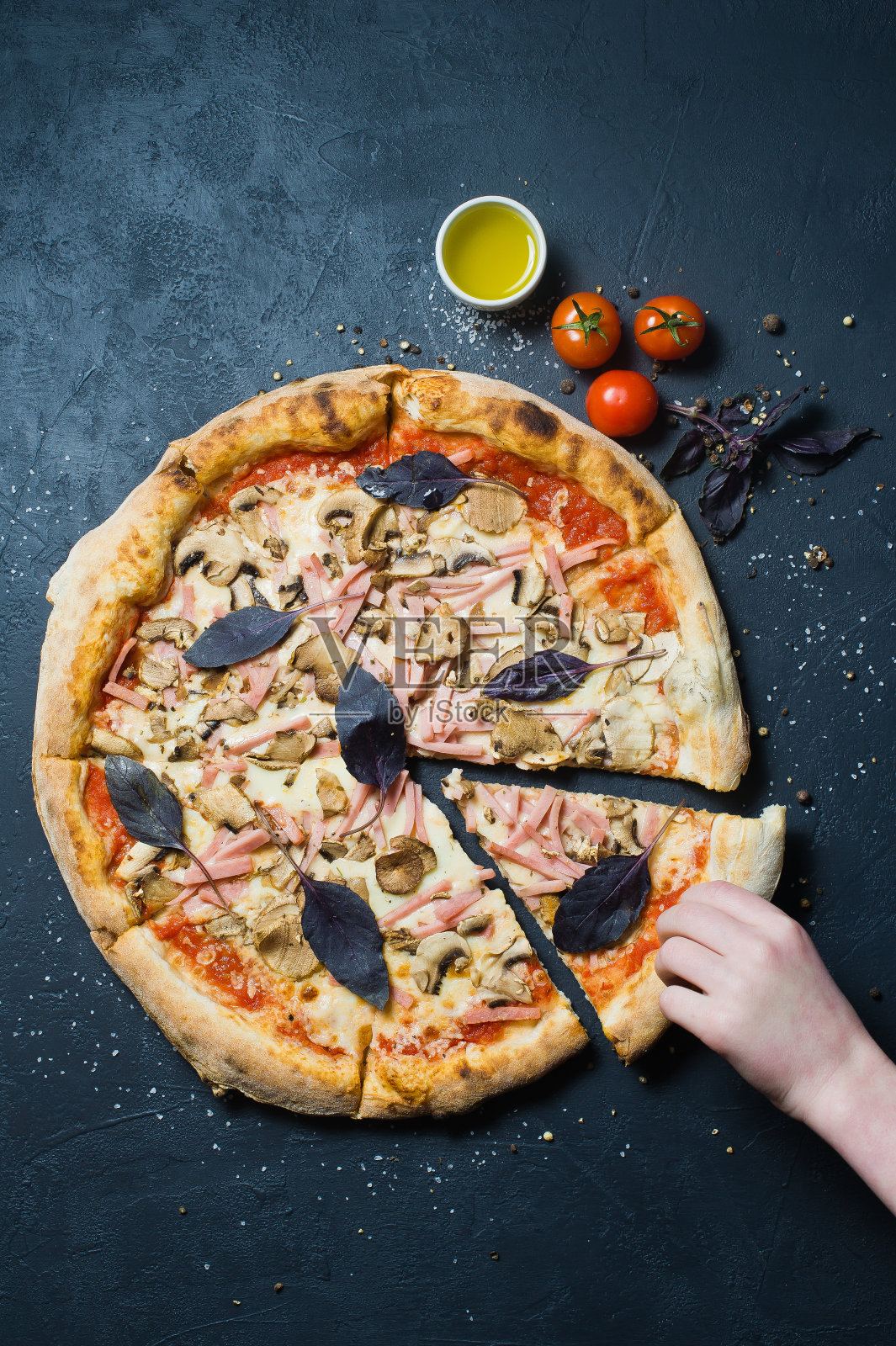 孩子拿了一片有火腿、蘑菇和罗勒的披萨。照片摄影图片