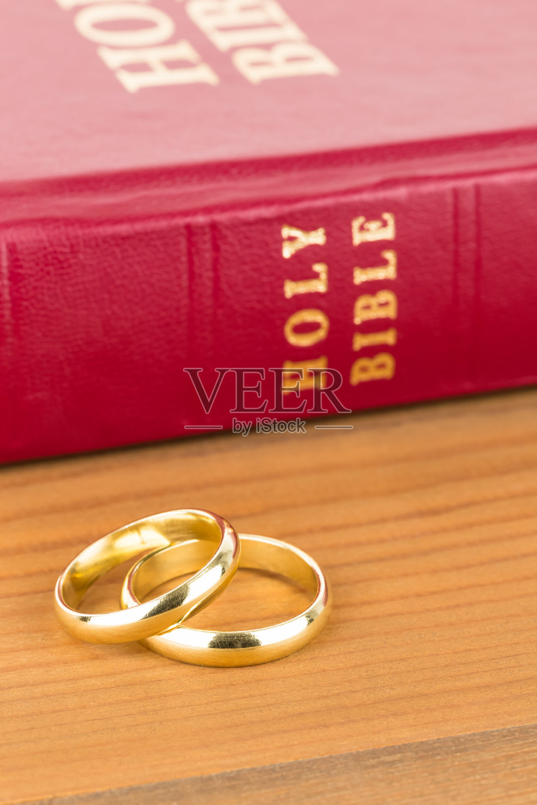 木制的桌子上放着金婚戒和红色的圣经照片摄影图片