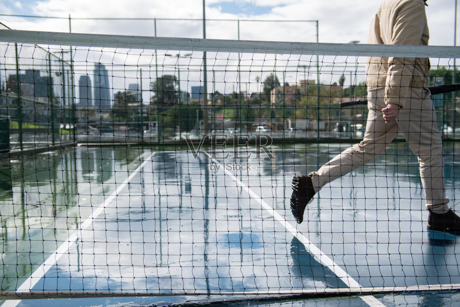 一名男子撑着伞走过潮湿的网球场照片摄影图片