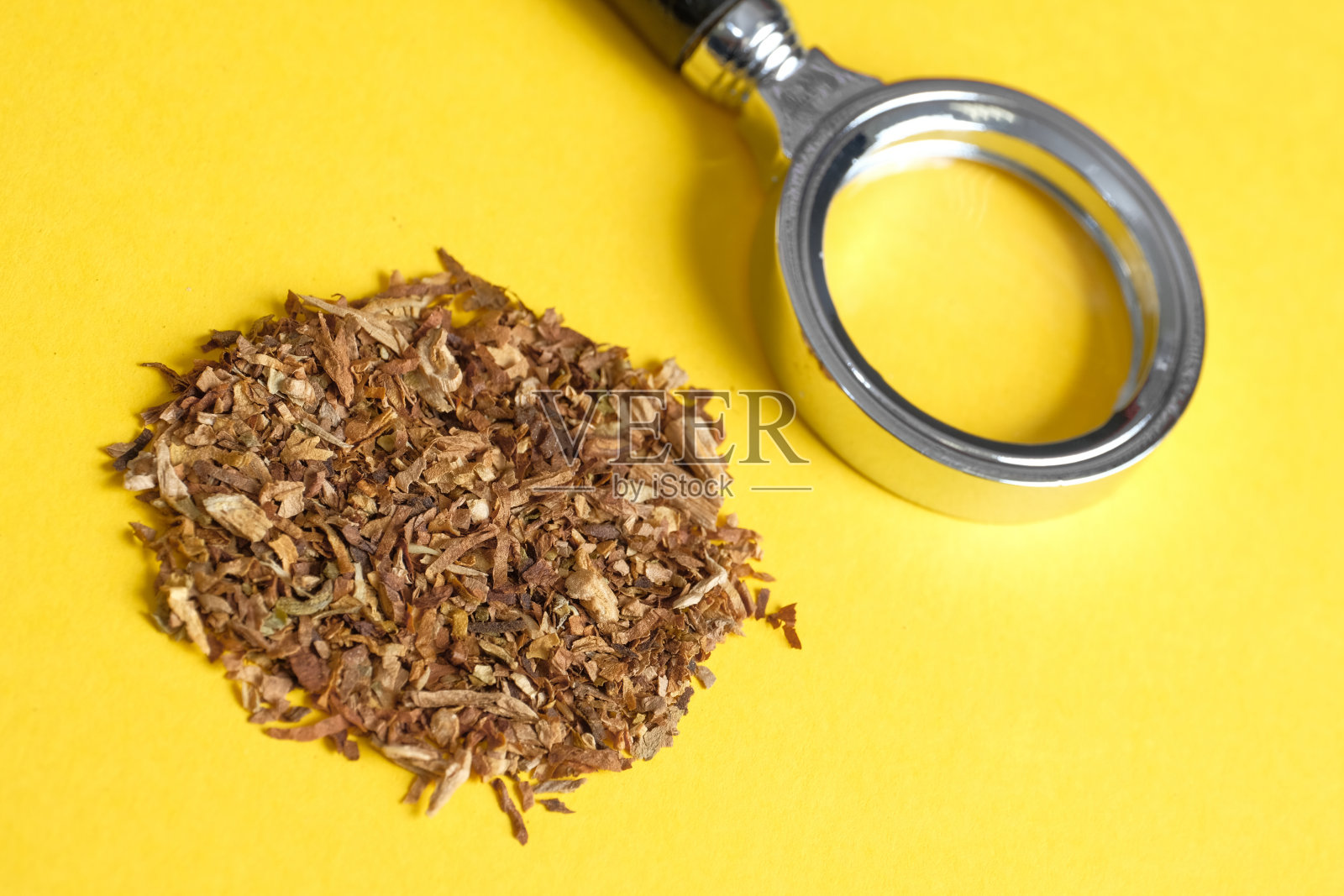 烟草危害的概念研究。黄色背景上的放大镜和一把烟草。照片摄影图片