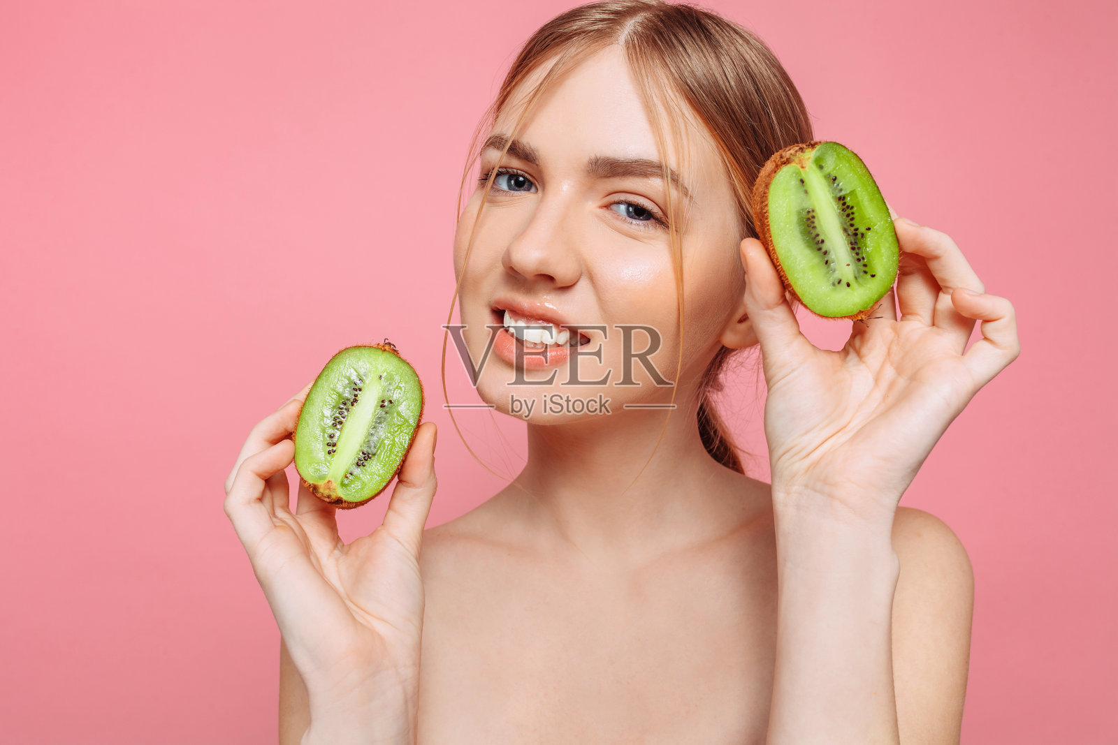 迷人的女孩拿着几维果片,在粉红色的背景上。自然美景照片摄影图片