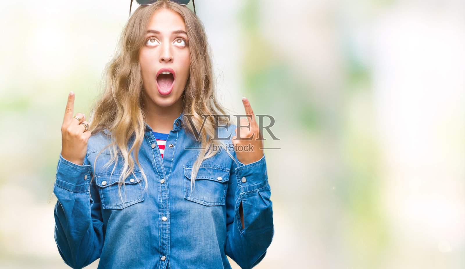 美丽的年轻的金发女人戴着太阳镜在孤立的背景惊讶和惊讶的看着和指向手指和举起的手臂。照片摄影图片