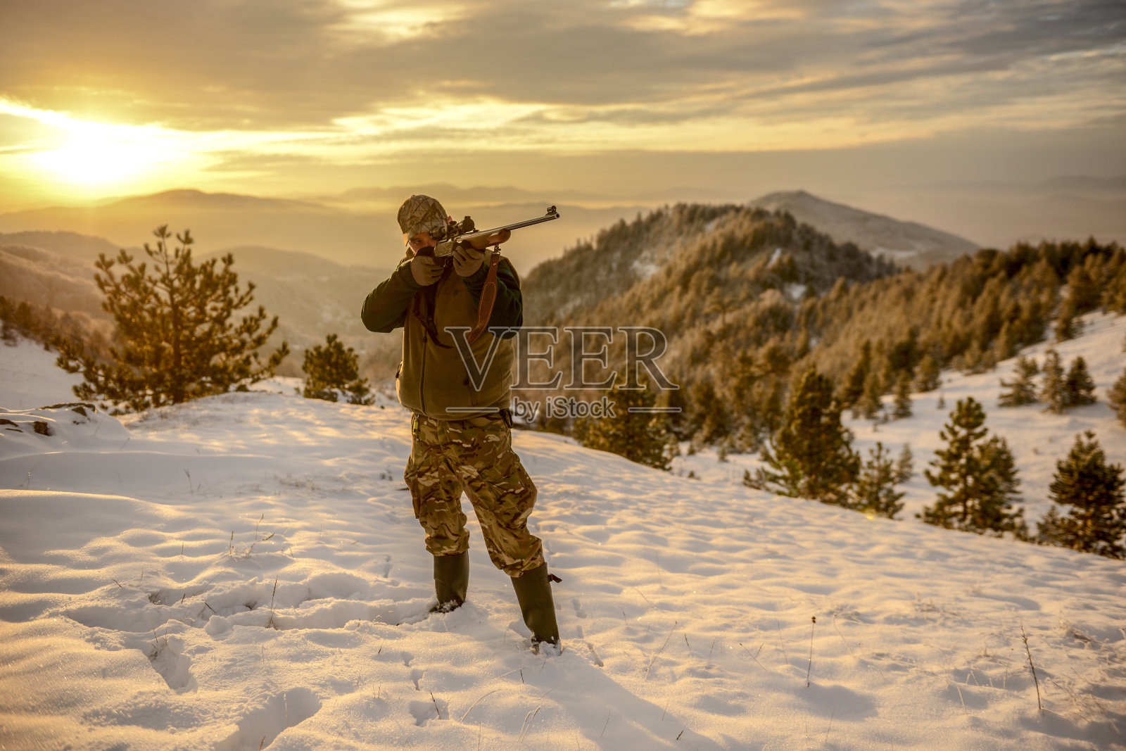日出时,猎人将步枪瞄准白雪覆盖的山谷照片摄影图片