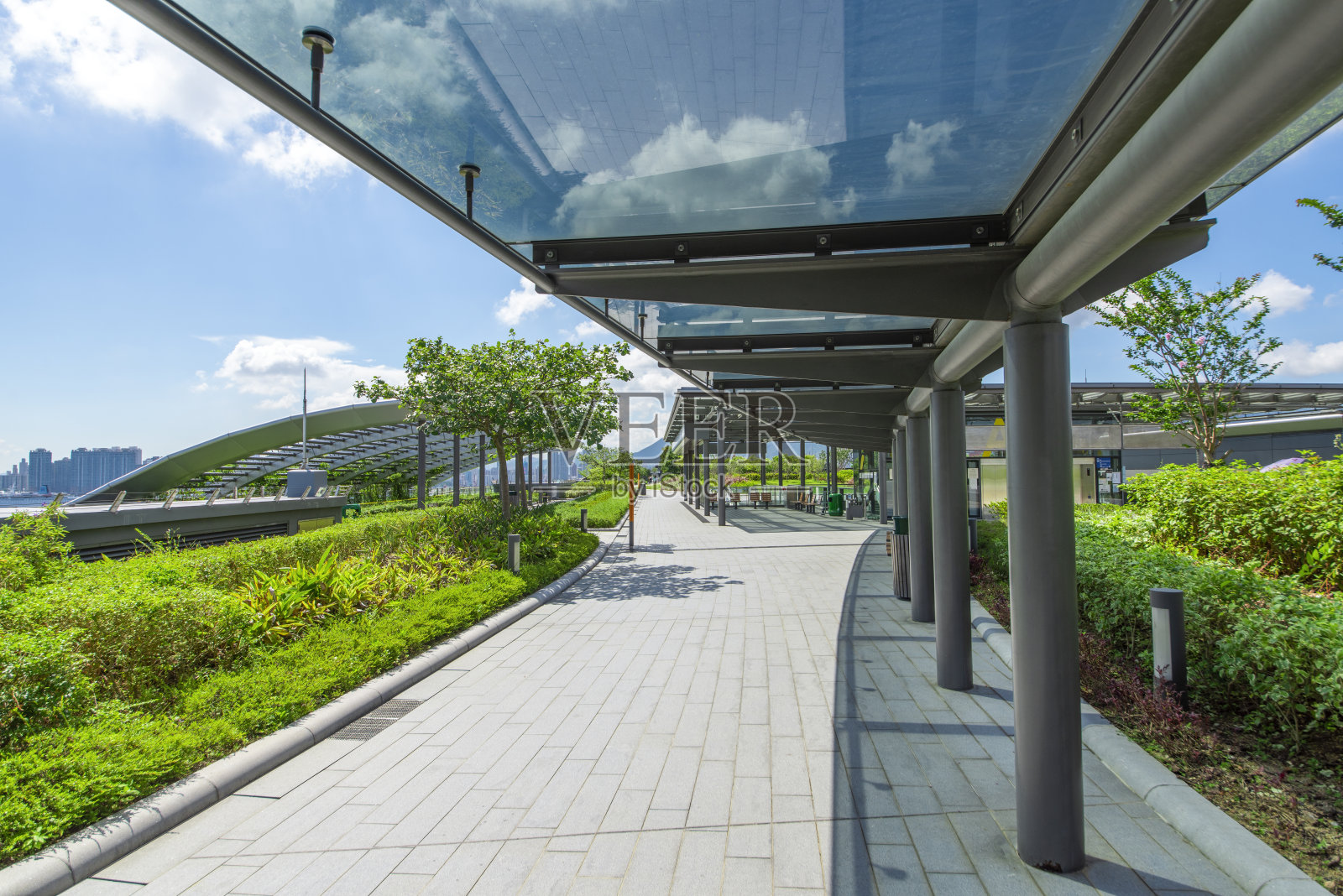 蓝天白云下的现代公园玻璃遮阳廊。照片摄影图片