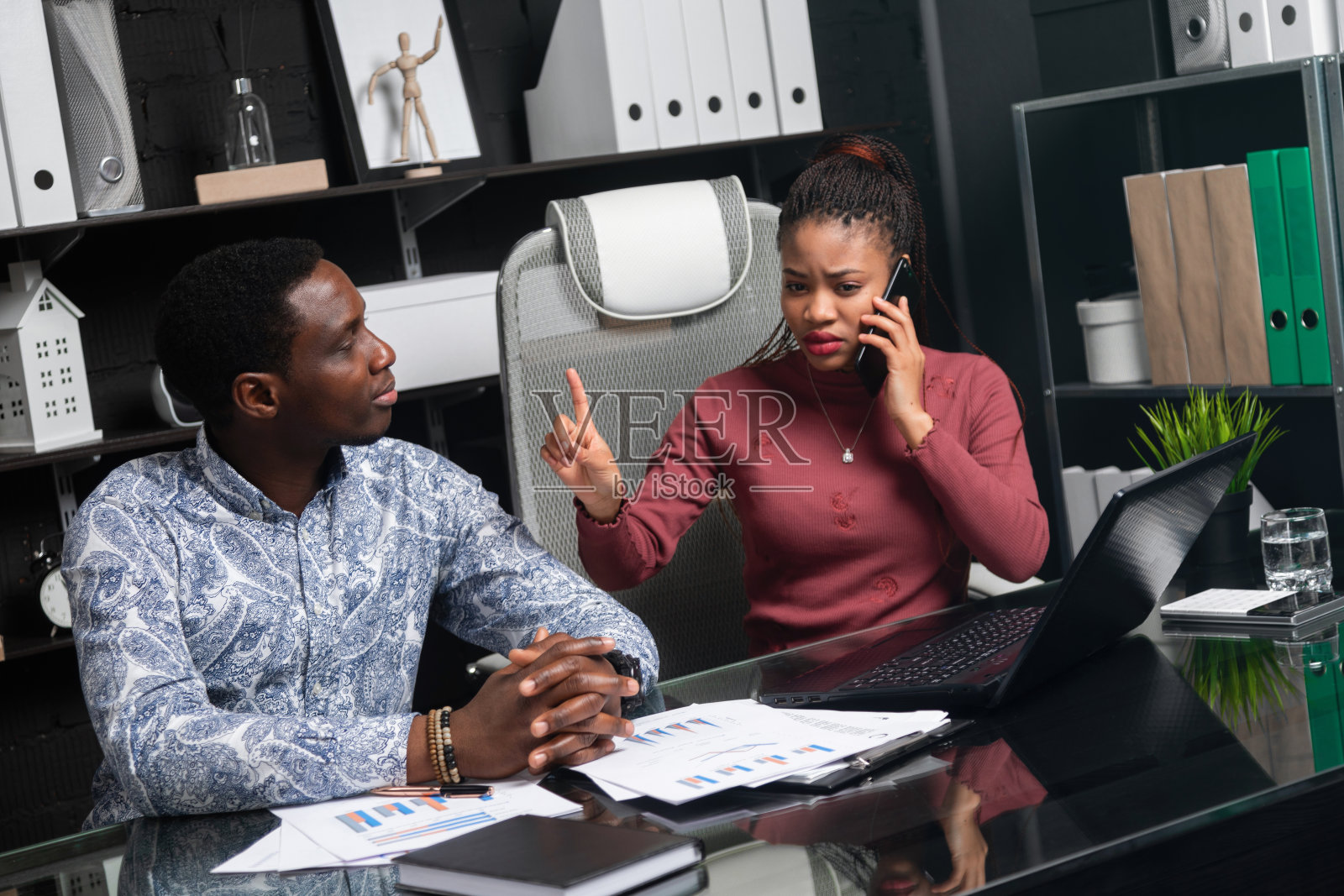 年轻的女孩接了电话,向这个男人展示了他坐在办公室的桌子旁等着的迹象照片摄影图片