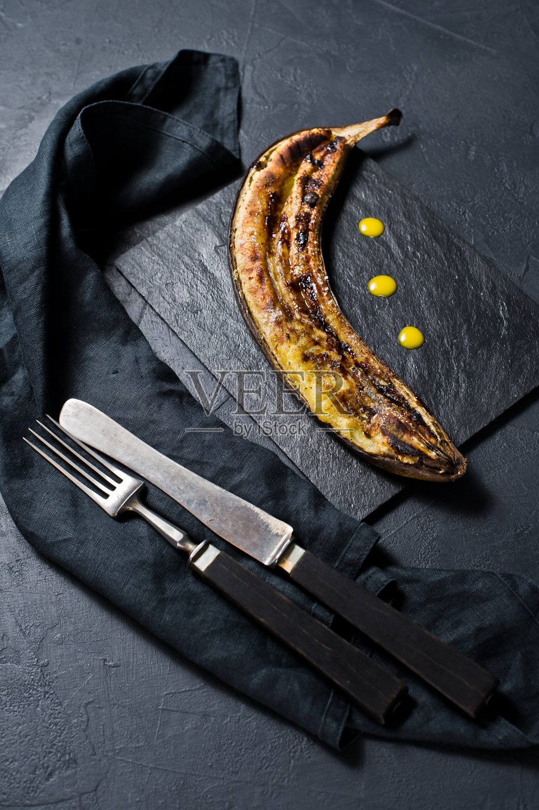 黑石板上的蜂蜜炒香蕉。黑色背景,俯视图,特写。照片摄影图片