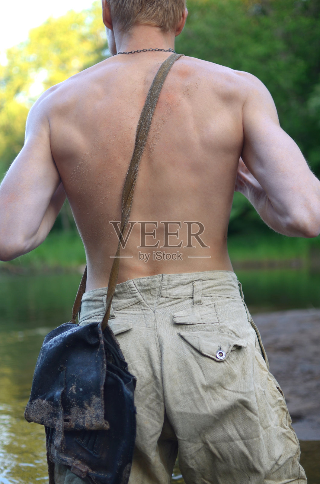 一名身穿旧军装、没有穿衬衫的年轻人背对着镜头站着照片摄影图片