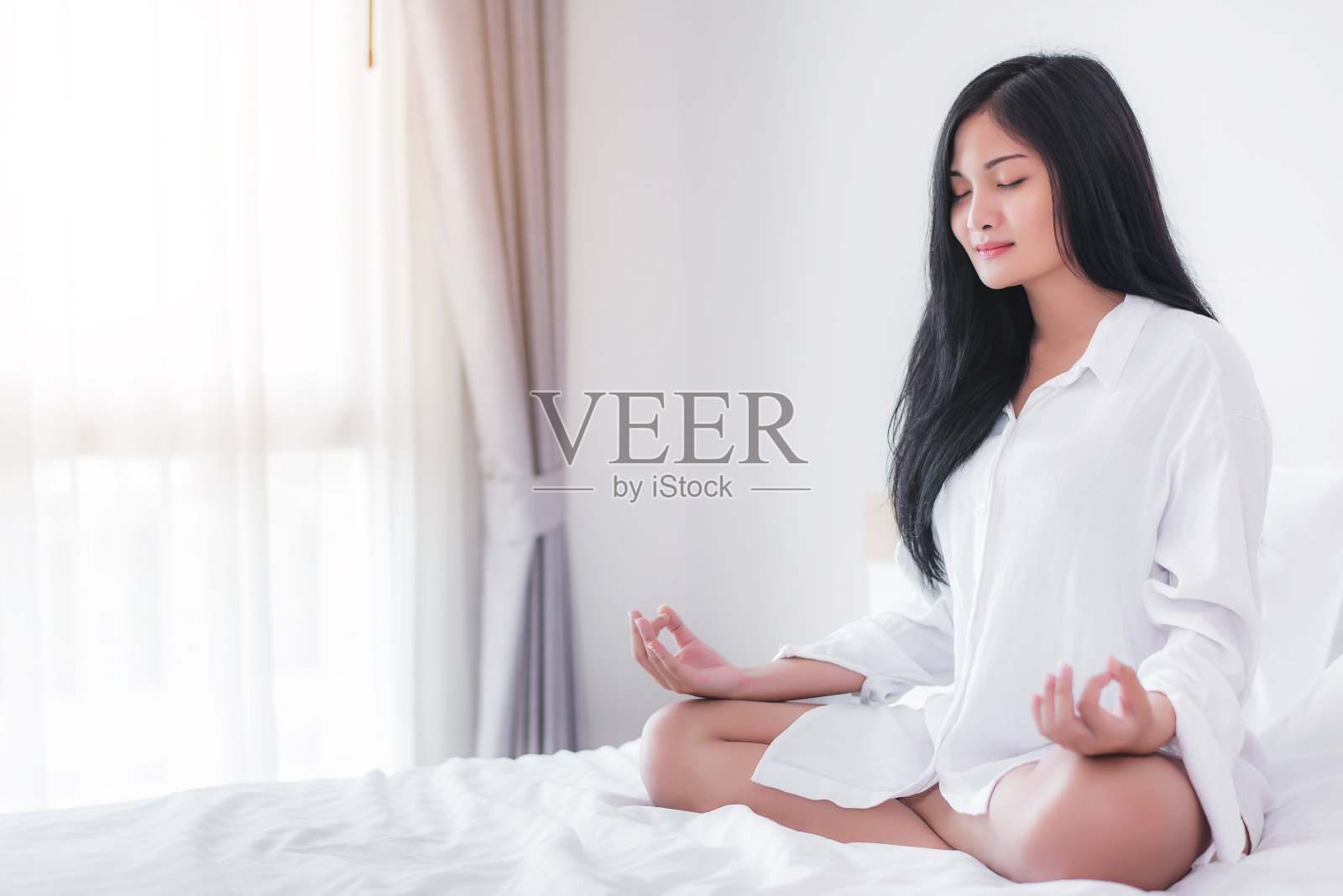 年轻迷人的亚洲女人在卧室的床上练习瑜伽。照片摄影图片