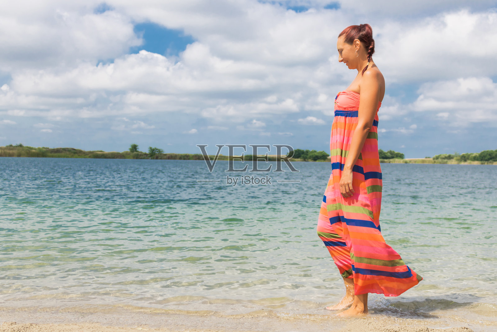 赤脚的女人在夏天的裙子在海滩上走过水。照片摄影图片