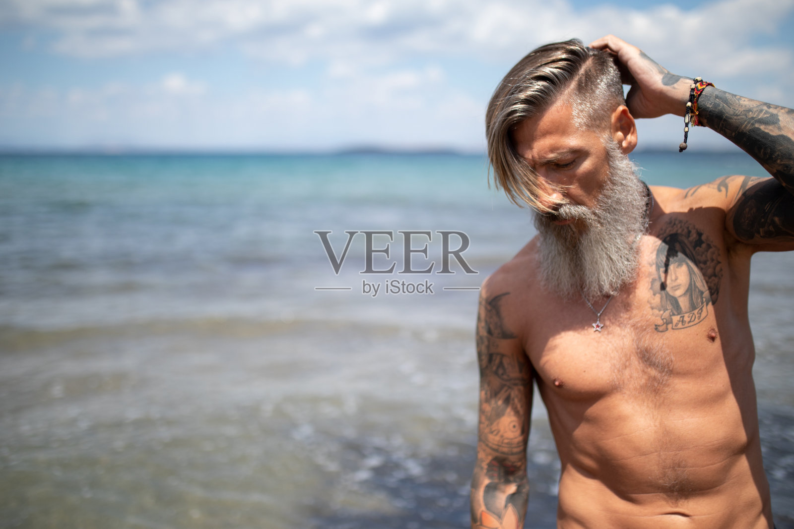 有魅力的胡子和纹身的成熟男子站在海滩上照片摄影图片