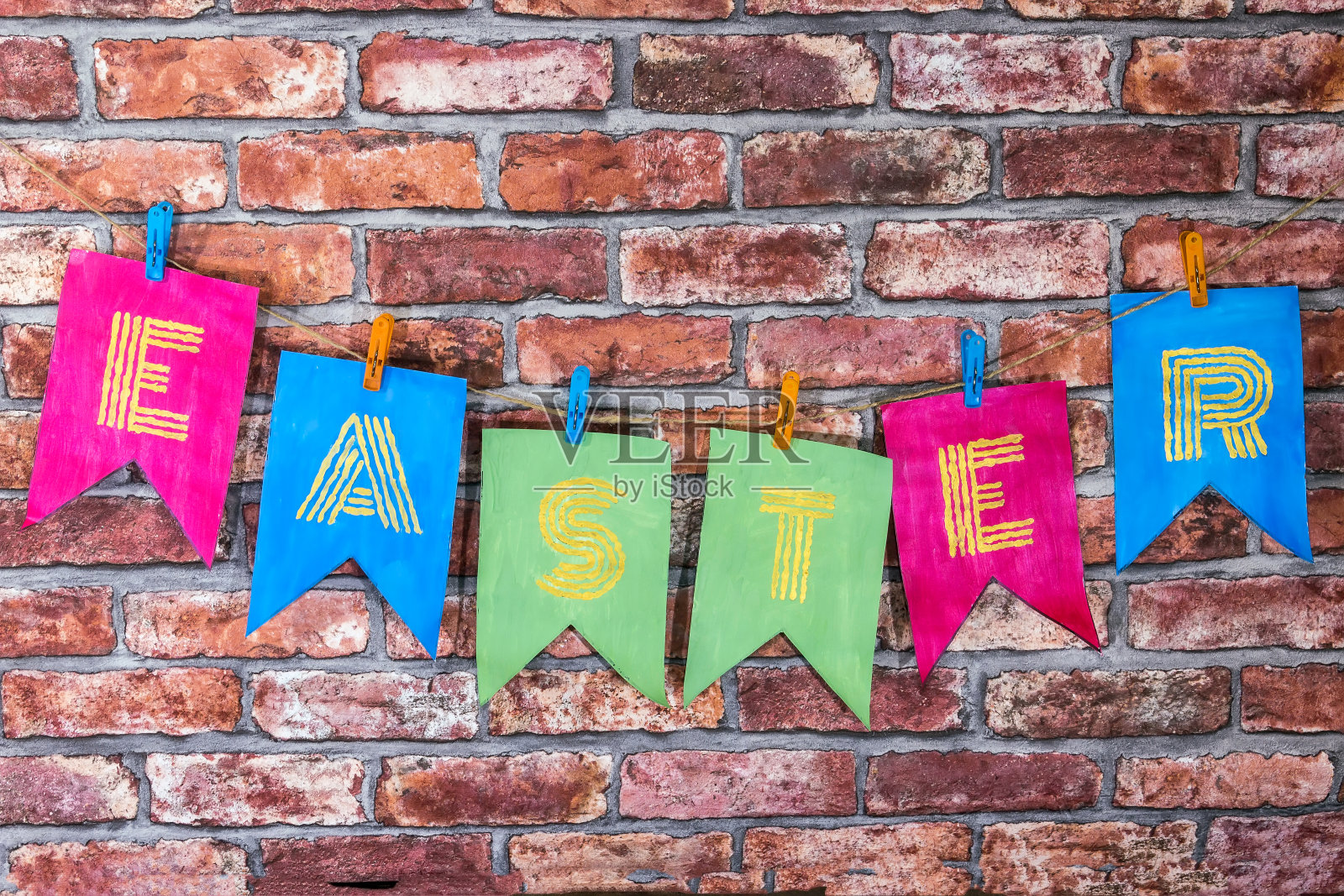 五颜六色的手工旗帜上写着复活节的字母、题词,贴在红砖墙上照片摄影图片