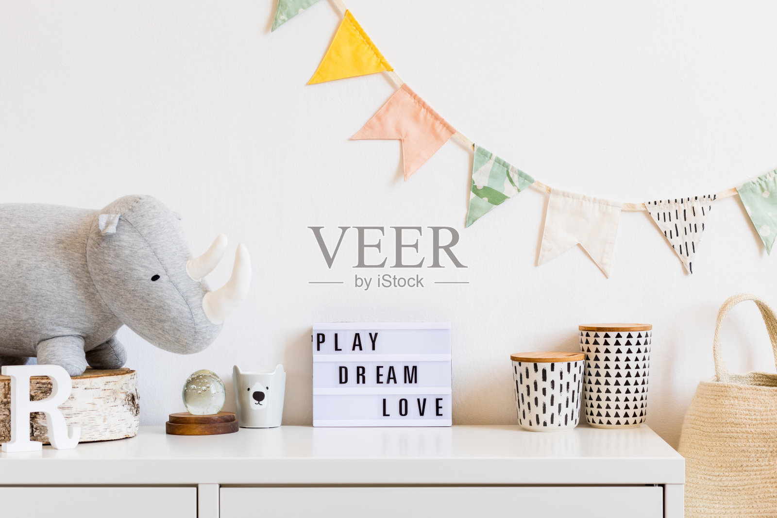 现代斯堪的那维亚新生儿室有毛绒犀牛,设计盒子,模拟黑板和自然篮子。白色的背景墙上挂着棉花旗。时尚舒适的室内设计。照片摄影图片