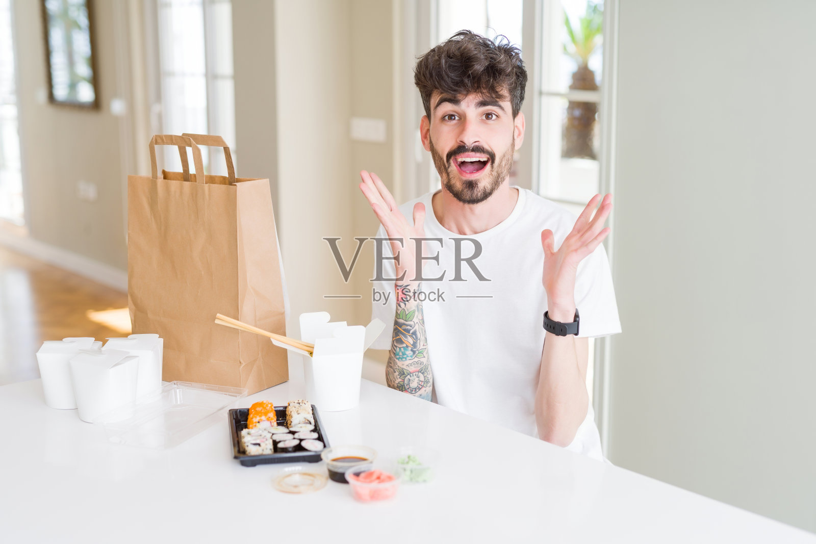 一名年轻人吃着外卖的亚洲寿司,举起手臂,睁大眼睛,兴奋地尖叫着,疯狂地庆祝成功。赢家的概念照片摄影图片