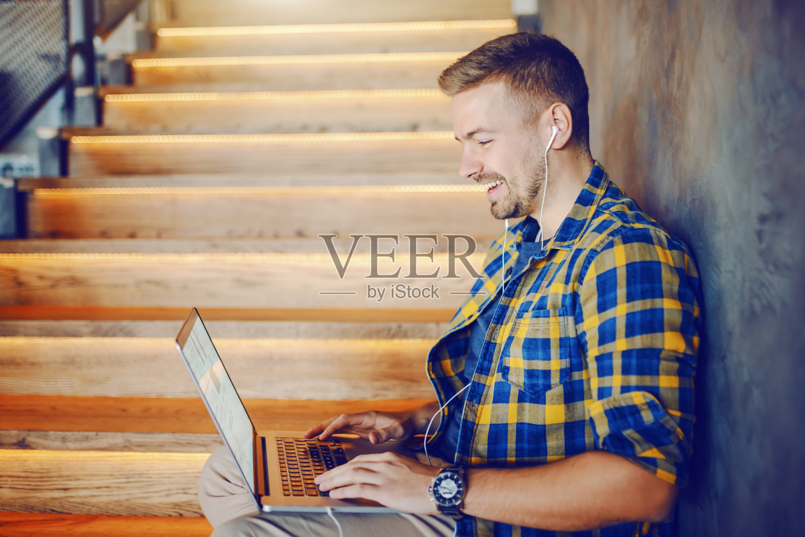 微笑的白人英俊男子在格子衬衫坐在咖啡馆的楼梯上,使用笔记本电脑工作。照片摄影图片