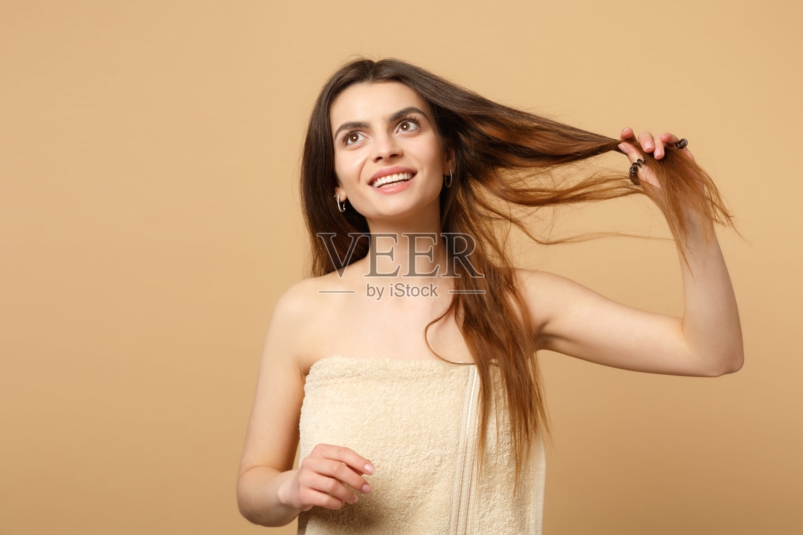 近距离黑发半裸女人20多岁与完美的皮肤,裸妆孤立在米色粉彩墙背景,工作室肖像。护肤保健美容程序概念。模拟拷贝空间。照片摄影图片