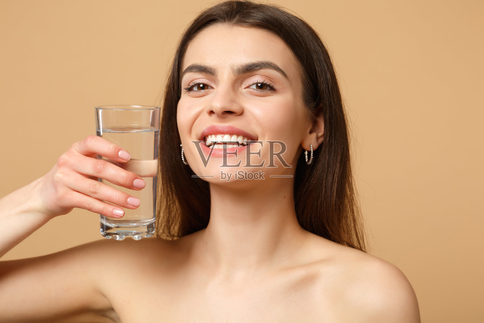 近距离黑发半裸女人20多岁与完美的皮肤裸化妆玻璃水隔离在米色粉彩墙背景,工作室肖像。保健美容程序概念。模拟拷贝空间。照片摄影图片