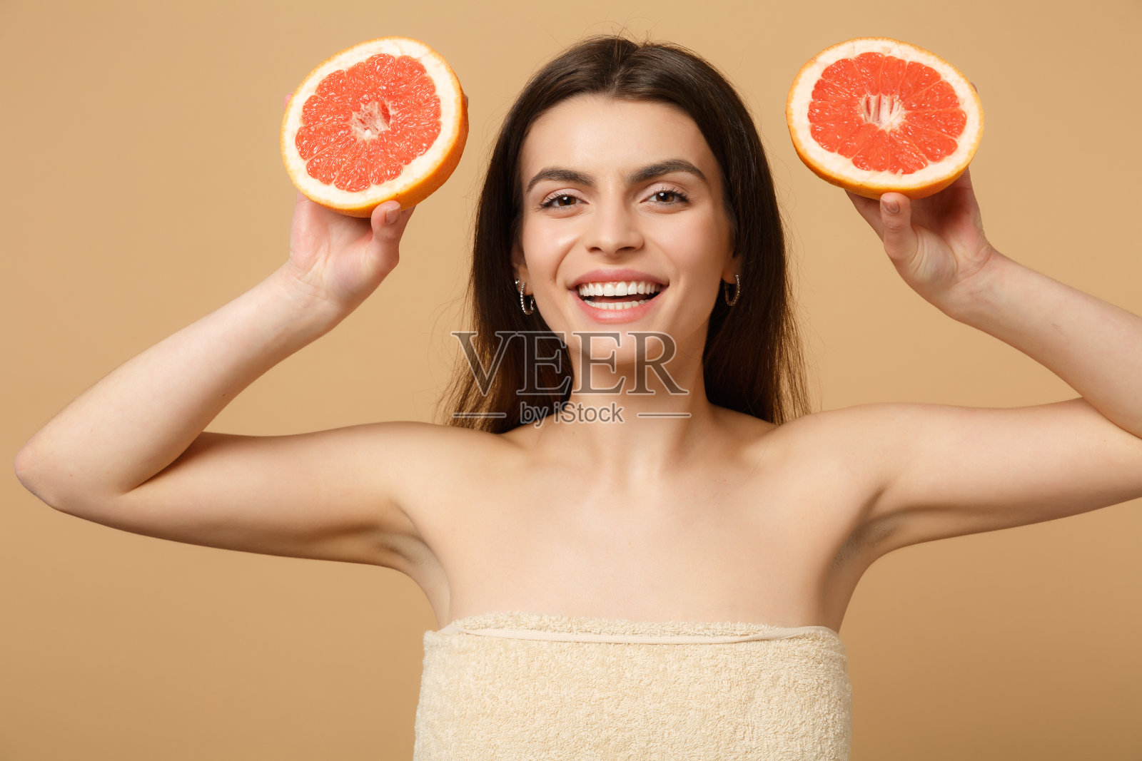 近距离美丽的女人20多岁与完美的皮肤化妆hold葡萄柚孤立的米色蜡笔墙背景工作室肖像。保健美容程序概念。模拟拷贝空间照片摄影图片