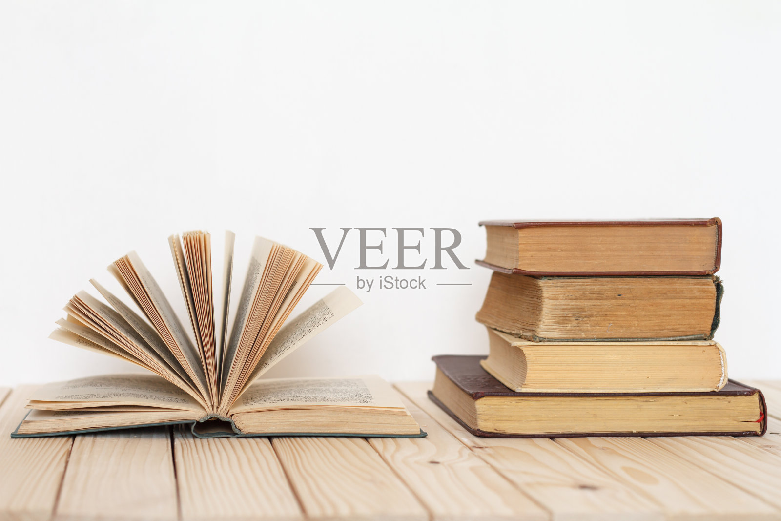 一本打开的书,在一堆旧书旁边,靠着一堵白色的墙。照片摄影图片