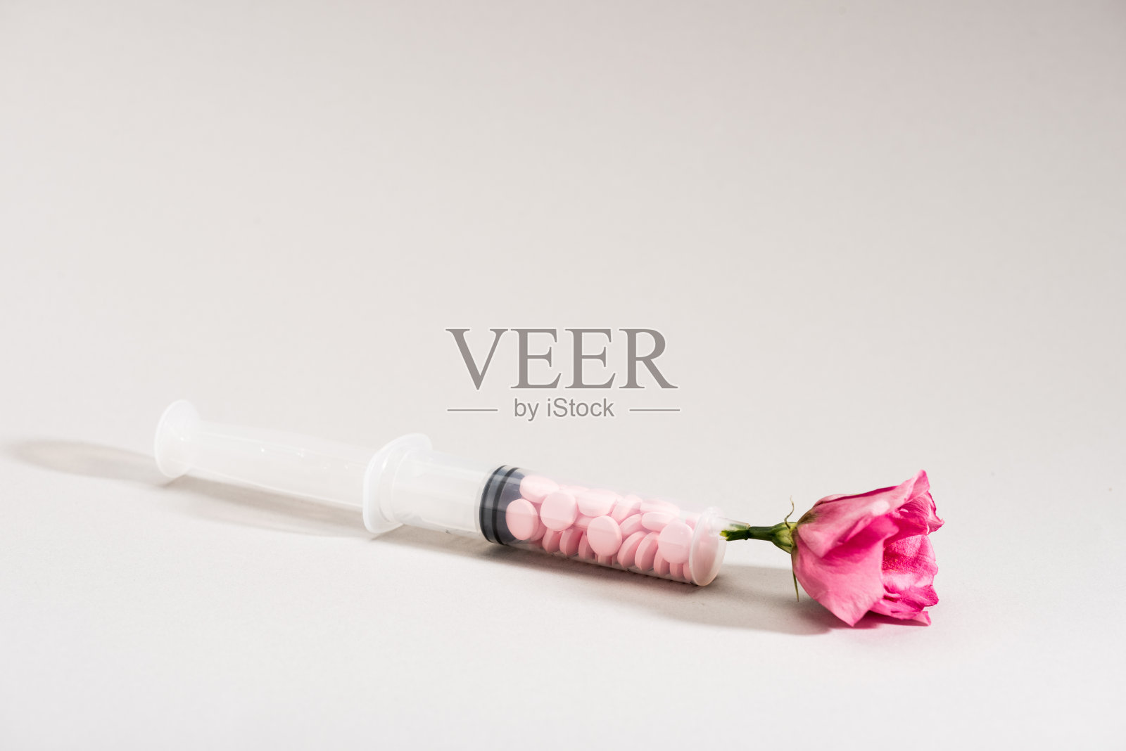 工作室拍摄的粉红色的花,注射器和药丸在灰色照片摄影图片