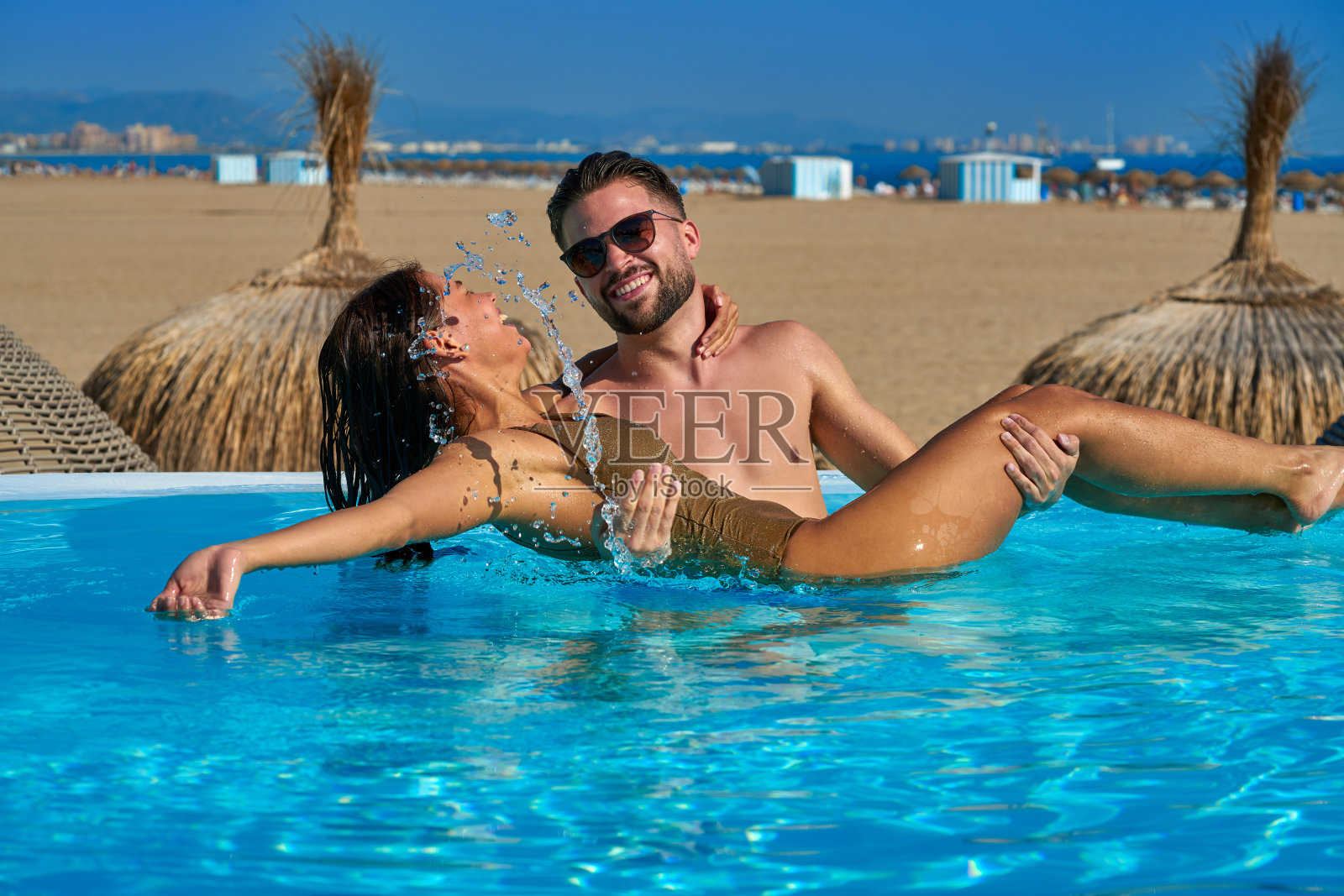 一对游客夫妇在沙滩上的无限游泳池洗澡照片摄影图片
