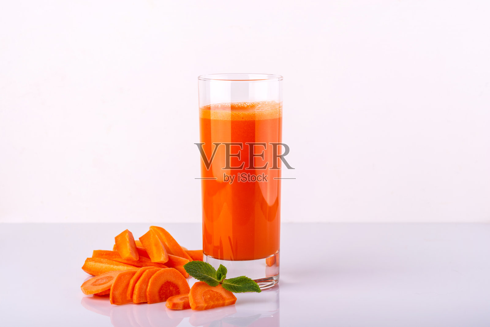 一杯胡萝卜汁,白色背景上有几块胡萝卜。生的胡萝卜饮料照片摄影图片
