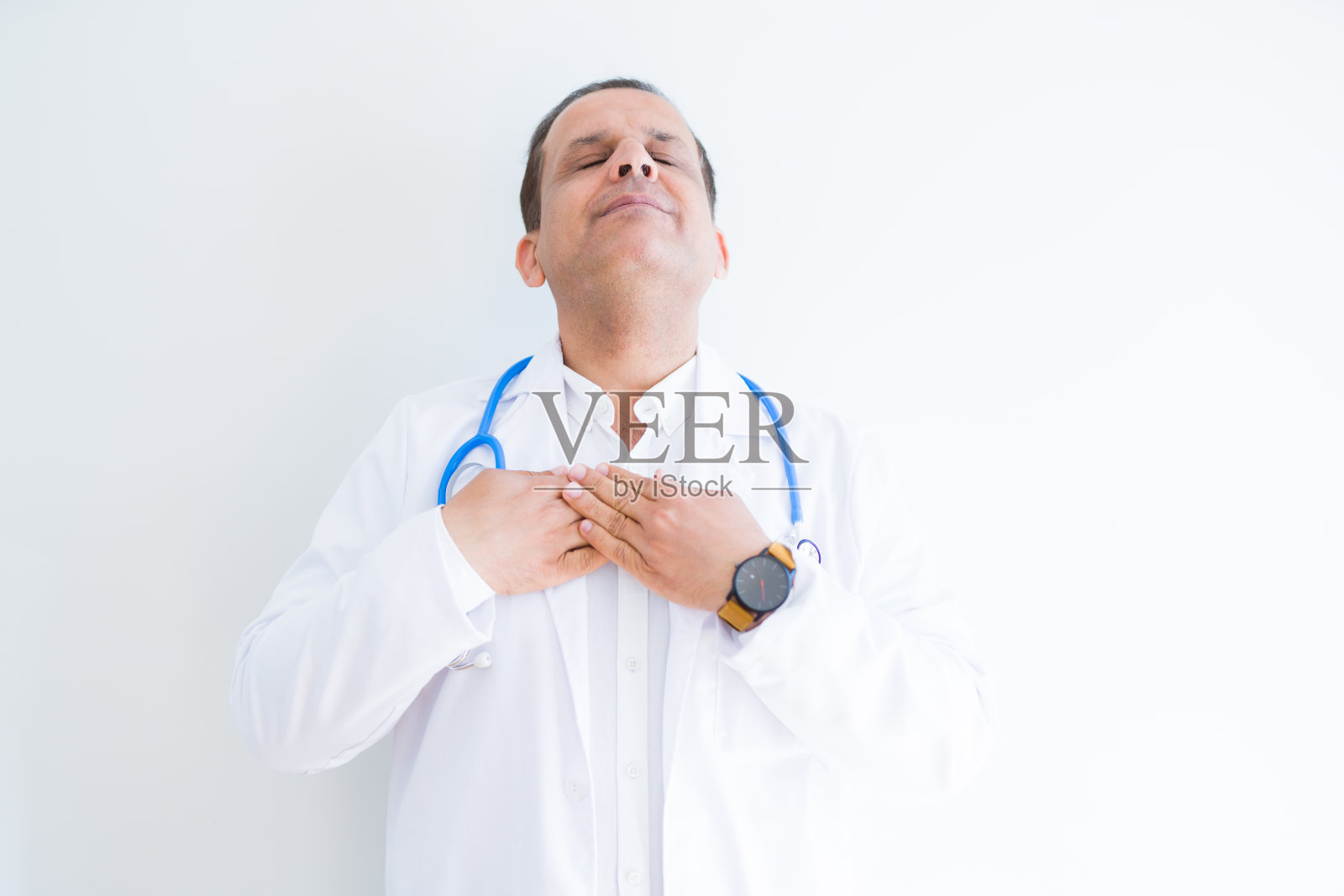 中年医生男子穿着听诊器和医疗外套在白色的背景微笑,双手放在胸前,闭上眼睛和感激的手势在脸上。健康的概念。照片摄影图片