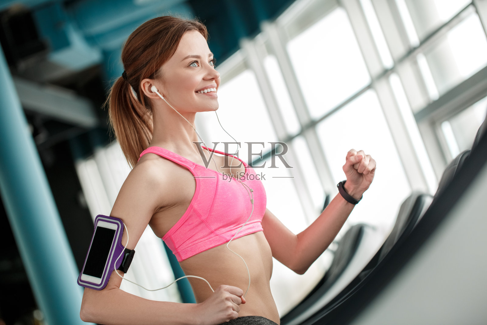 年轻女孩在健身房以健康的生活方式在跑步机上跑步,戴着臂圈和耳机听着欢快的音乐照片摄影图片
