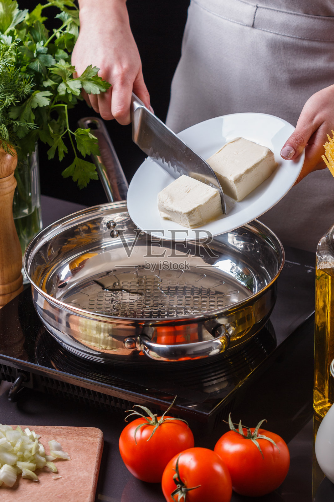 一位穿着灰色围裙的年轻妇女在煎锅里放黄油照片摄影图片