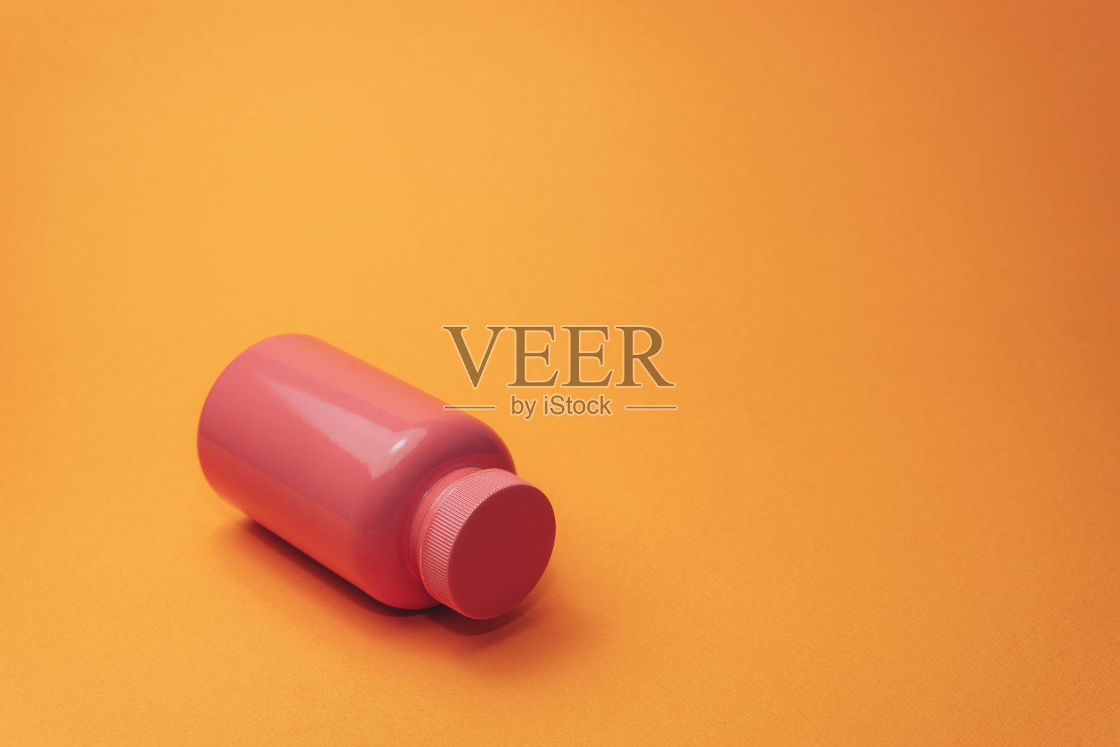 橙色背景的粉色药丸瓶。照片摄影图片