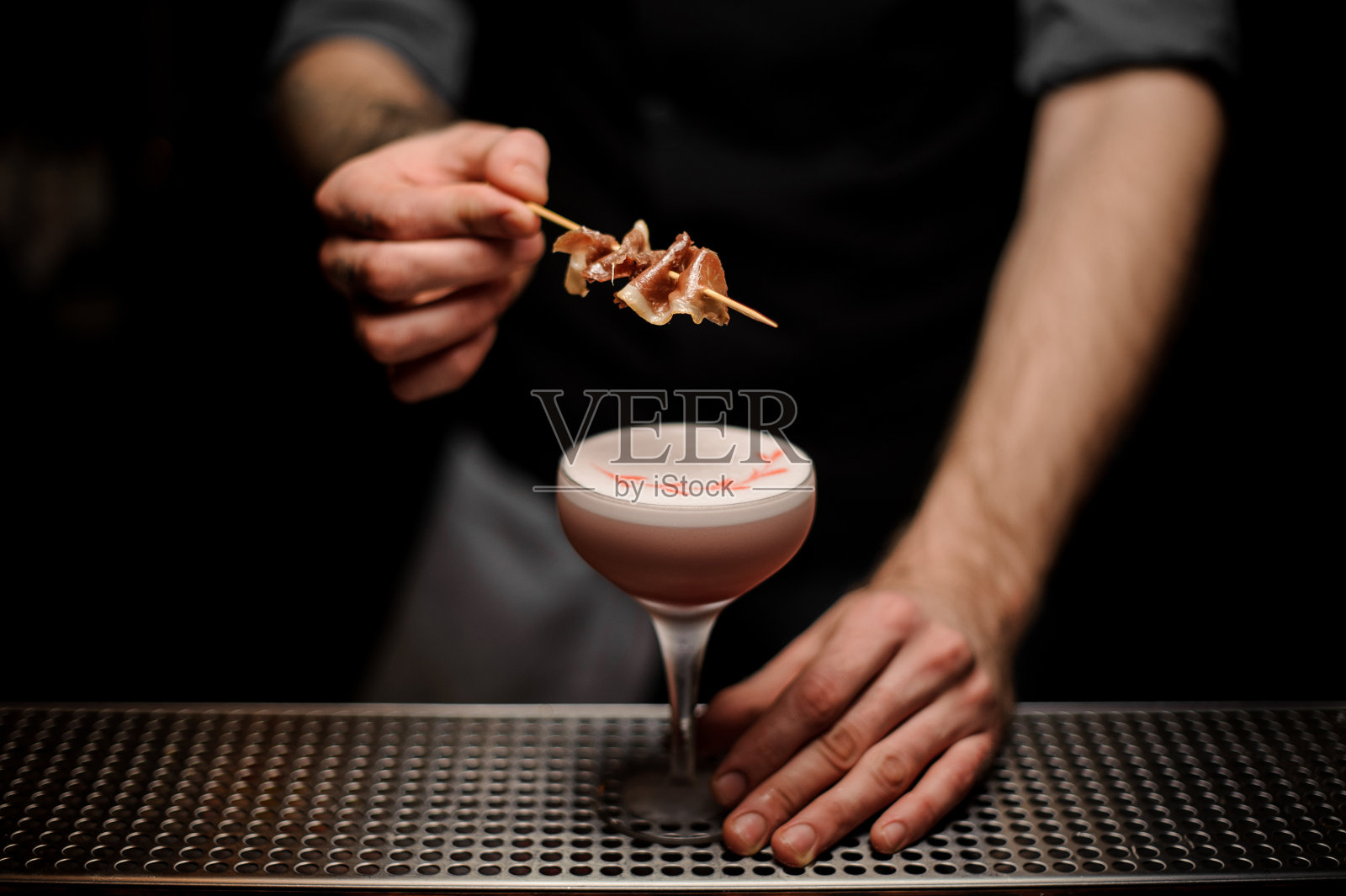 男酒保用白色泡沫装饰粉红色鸡尾酒和熏肉串照片摄影图片