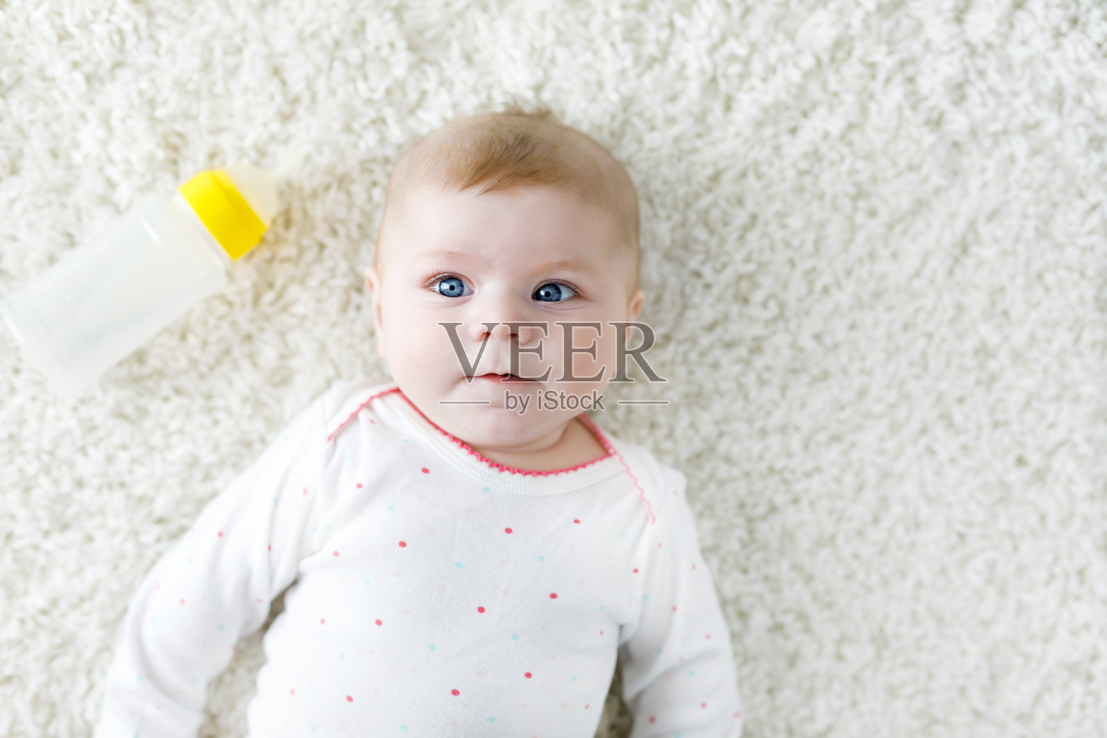 可爱可爱的新生女婴抱着奶瓶,喝着配方奶。新生儿,小女孩躺在白色的背景上。照片摄影图片