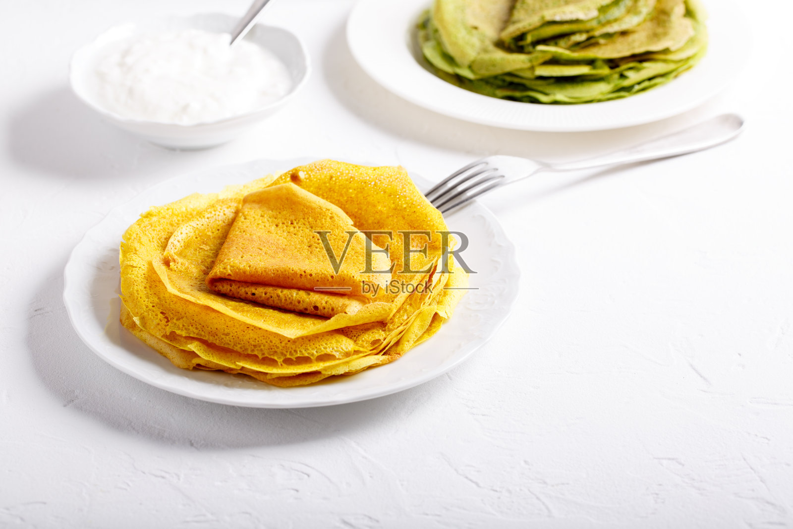 黄色和绿色的煎饼放在白色的盘子里。白色背景上的姜黄色的菠菜薄饼。副本的空间。照片摄影图片