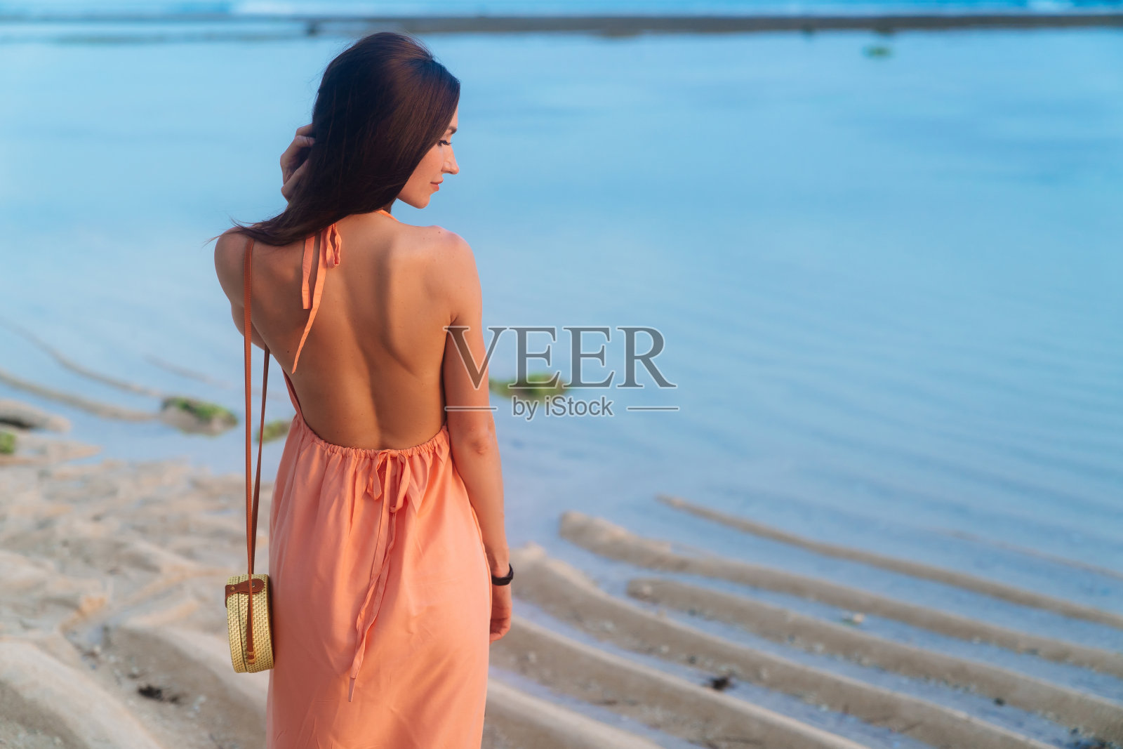 后视图黑发女孩与长头发在沙滩裙和柳条袋在长带子在海滩摆姿势照片摄影图片