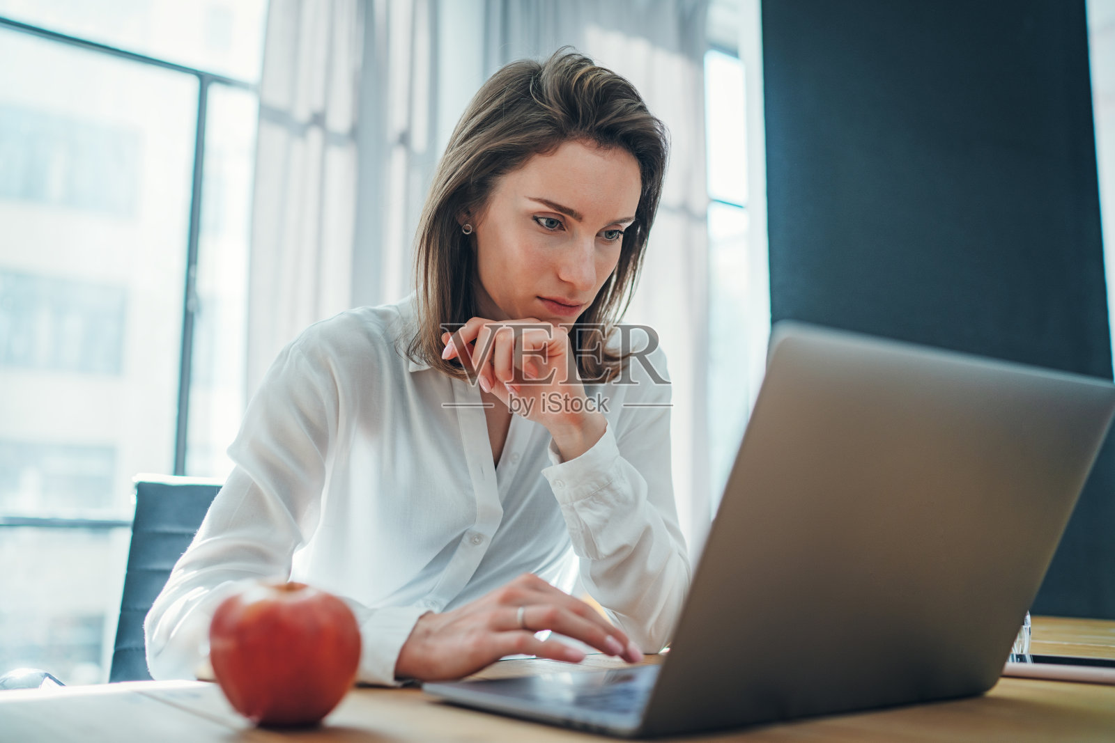 年轻的女企业家在办公室工作过程中使用移动笔记本电脑寻找新的商业解决方案。模糊的背景。照片摄影图片