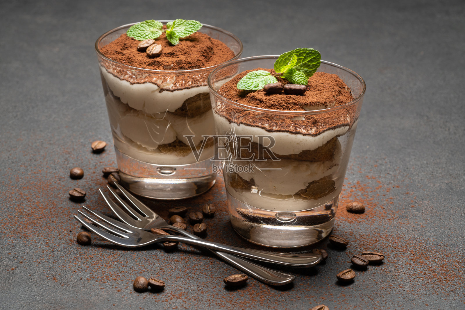 两份经典的提拉米苏甜点放在一个玻璃杯里,背景是深色的混凝土照片摄影图片