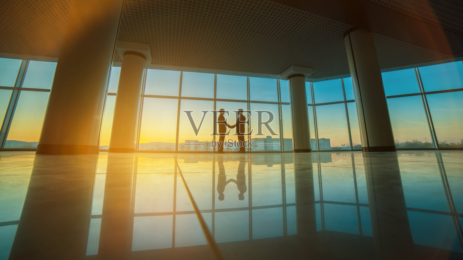 夕阳背景下,两位商人在办公室里握手照片摄影图片