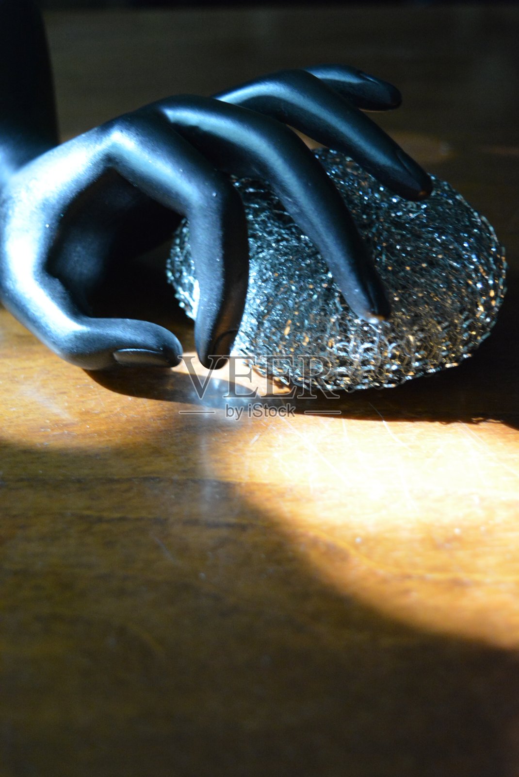 黑色的女性手雕像和金属海绵放在棕色的老式木桌上,上面有阳光的光线。照片摄影图片