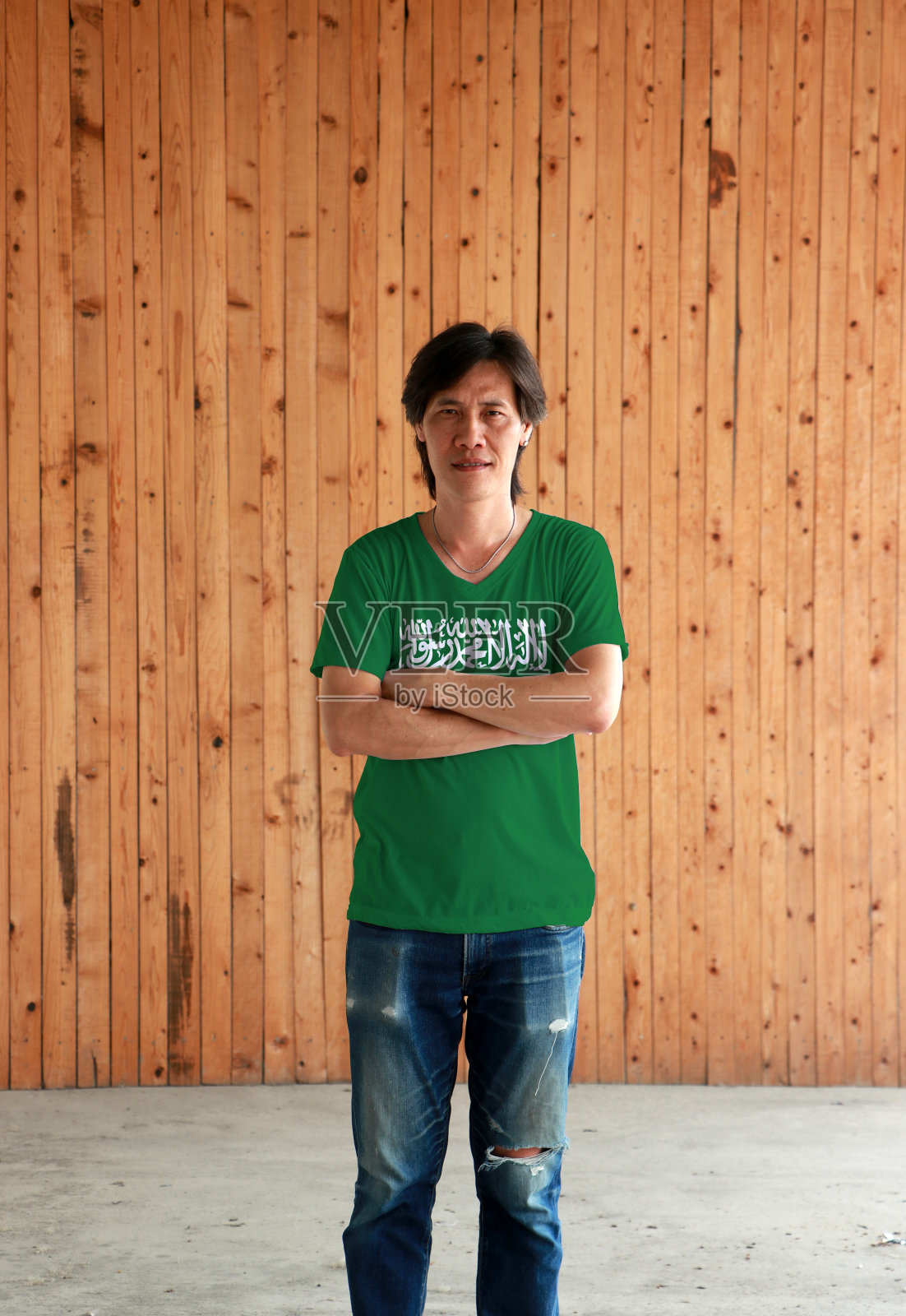 穿着沙特阿拉伯国旗颜色衬衫的男人,在木墙背景前交叉双臂照片摄影图片