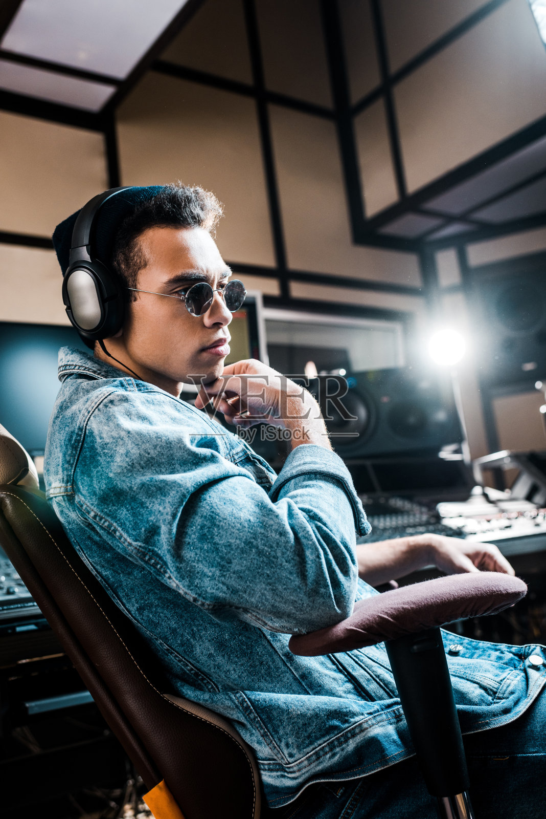 英俊严肃的混合种族声音制作人在太阳镜和耳机坐在录音室照片摄影图片