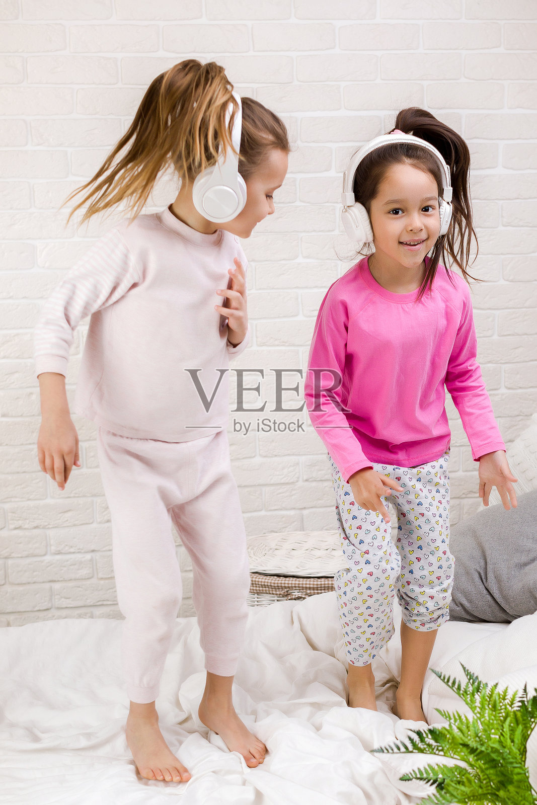 小女孩们戴着耳机听音乐,在床上跳舞。照片摄影图片