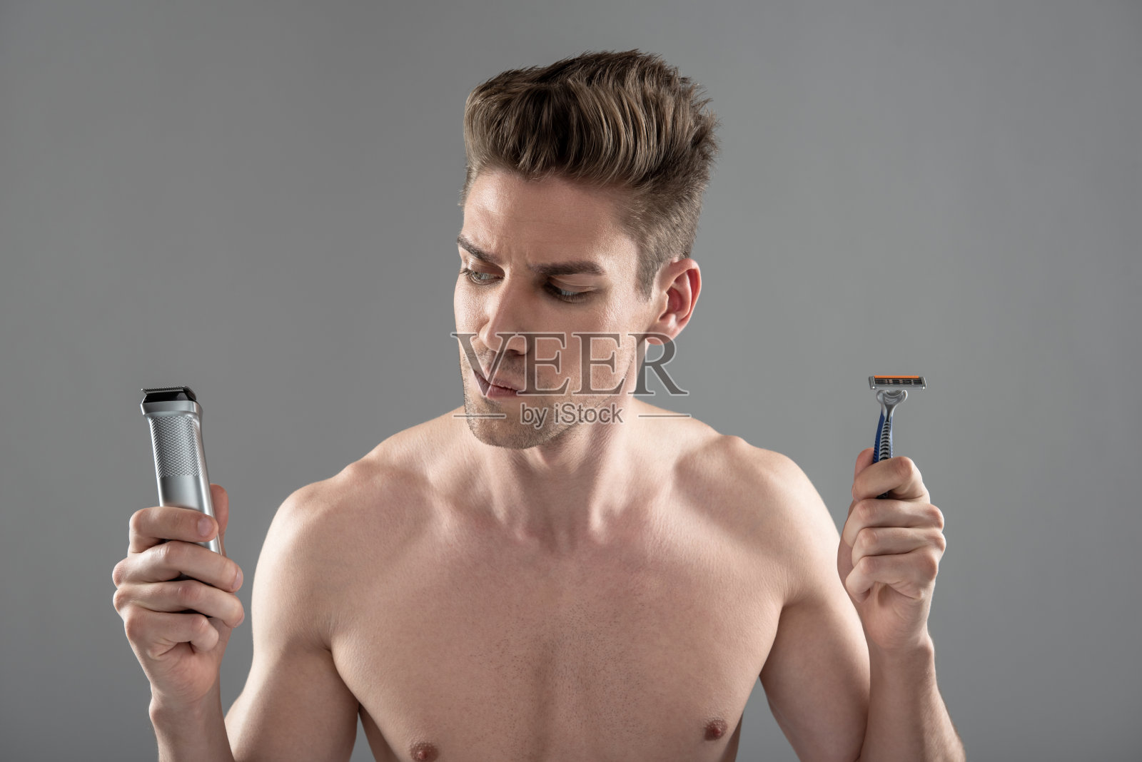 英俊的年轻人在剃须机和一次性剃须刀之间做出选择照片摄影图片